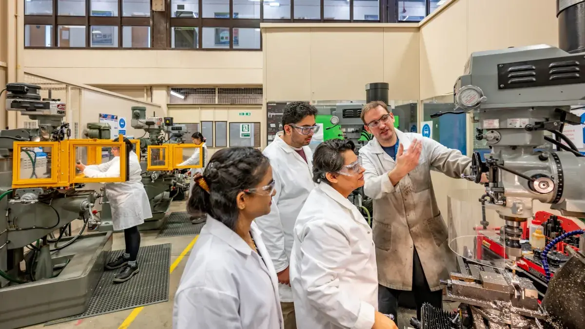 Three students in an engineering lab at Heriot Watt University are being shown how to use a machine