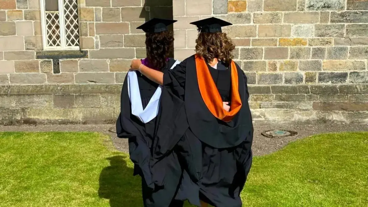 Two women in graduation robes face away from the camera, their arms around each other