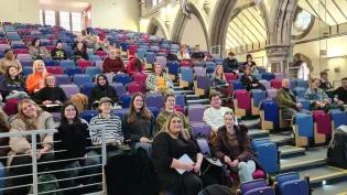A large group of students sat in a lecture hall smile for the camera