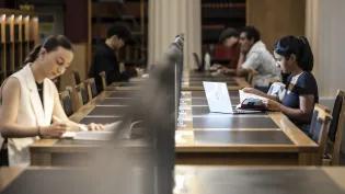 two students sit on either side of a long library table