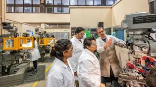 Three students in an engineering lab at Heriot Watt University are being shown how to use a machine