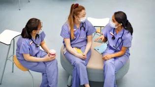 three women in purple scrubs and masks sit and chat