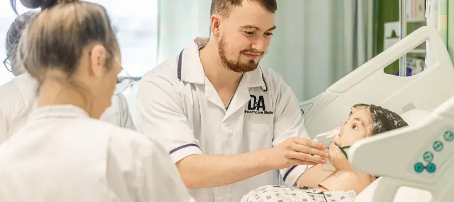A student in a nurses uniform works with a dummy patient on a hospital bed