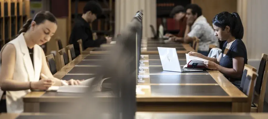 two students sit on either side of a long library table