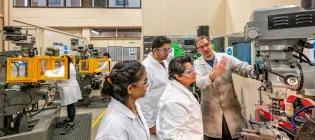 Three students in an engineering lab at Heriot Watt University are being shown how to use a machine