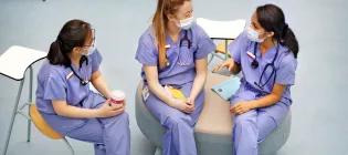 three women in purple scrubs and masks sit and chat