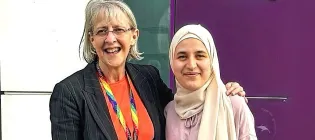 Two women smile at the camera, the older with her arm around the younger
