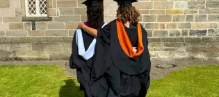 Two women in graduation robes face away from the camera, their arms around each other