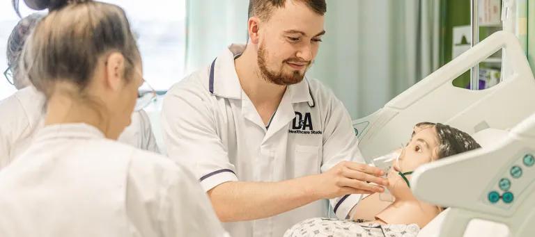 A student in a nurses uniform works with a dummy patient on a hospital bed