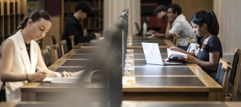 two students sit on either side of a long library table