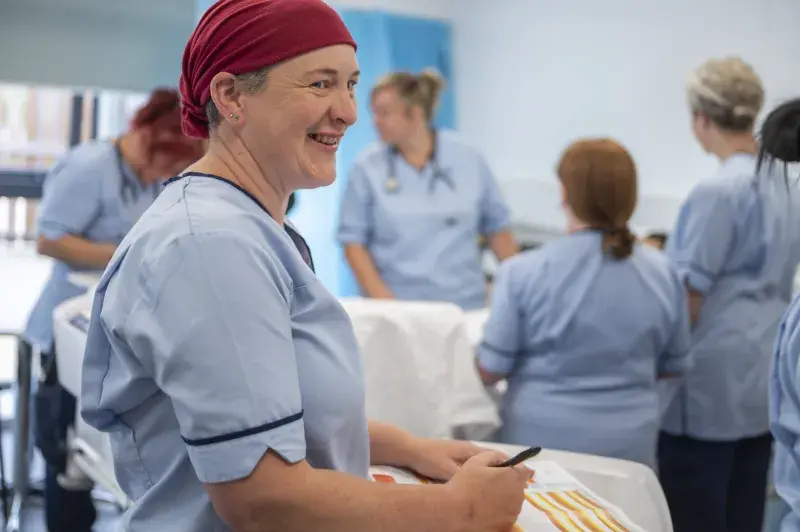 A student wearing nursing scrubs and a red head covering laughs while in a nursing class at Borders College
