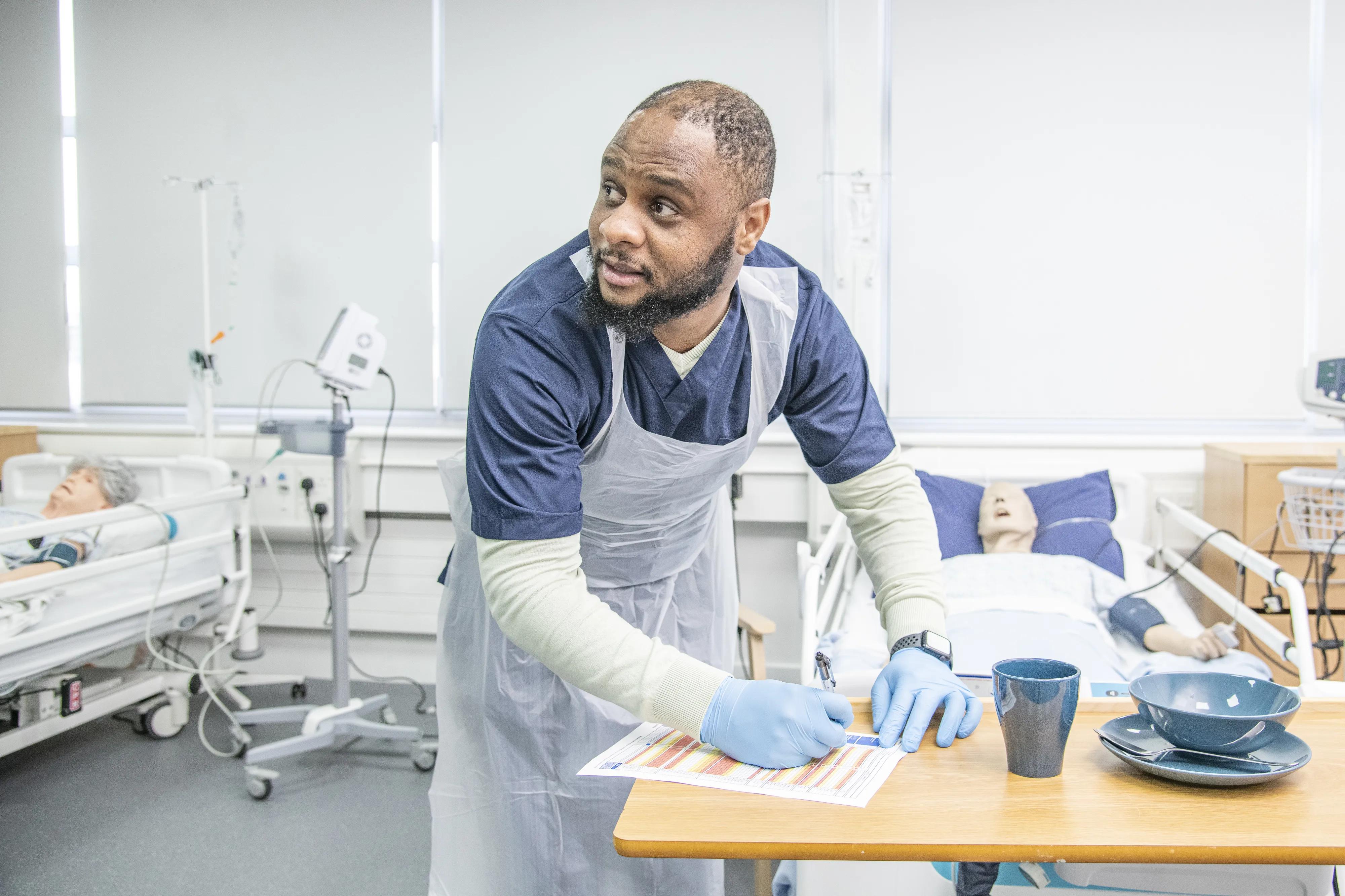 An Access to Nursing student at West Lothian College takes notes while wearing scrubs and PPE