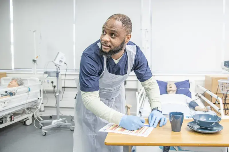 An Access to Nursing student at West Lothian College takes notes while wearing scrubs and PPE